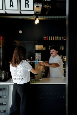Un comptoir de bar où une personne sert une boisson à une autre. On peut voir des bouteilles et des verres sur le comptoir.