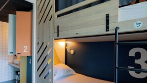 Een stapelbed met een houten hoofdbord, een bureau en een stoel in een kamer met een betegelde vloer.
