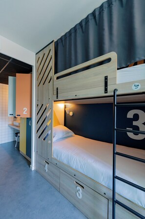 Een stapelbed met een houten hoofdbord, een bureau en een stoel in een kamer met een betegelde vloer.