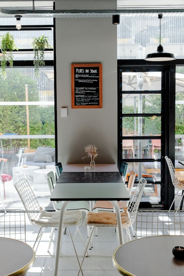 A café with a menu board, white chairs, and a view through large windows.