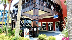 A multi-story building with a wooden staircase and balcony, surrounded by palm trees and greenery.