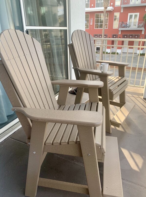 Two Adirondack chairs with a small table and a cup on the table, positioned on a balcony with a view of a building in the background. - Beautiful, 30A Cabana Breeze @ Gulf Place, Santa Rosa Beach, FL, Gulfview (Santa Rosa Beach)