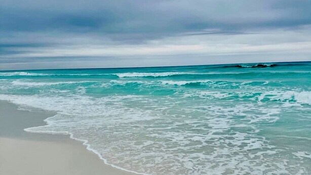 A beach with waves gently lapping onto the shore under a cloudy sky.
