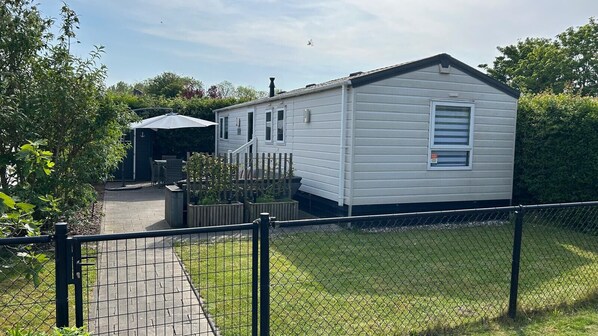 A small, single-story mobile home with a fenced yard and a covered outdoor seating area.