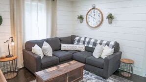 Una sala de estar moderna con un sofá modular, una mesa de centro de madera, un reloj de pared y una mesita auxiliar.