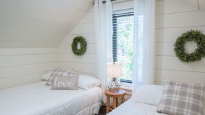 Un dormitorio con dos camas, una ventana con persianas, una lámpara sobre una mesita y dos coronas verdes en las paredes.