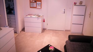 Une pièce de taille modeste, avec une armoire blanche, une petite table sur laquelle est posé un vase, et une porte ornée d’une horloge.