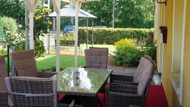 Un patio couvert aménagé avec des meubles en osier et une table en verre.