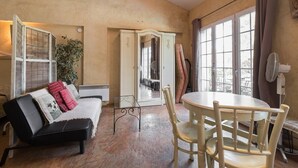 A cozy living room with a sofa, a dining table, and a view of the outdoors through large windows. - Gite Catalin à St Rémy de Provence (Saint-Rémy-de-Provence)