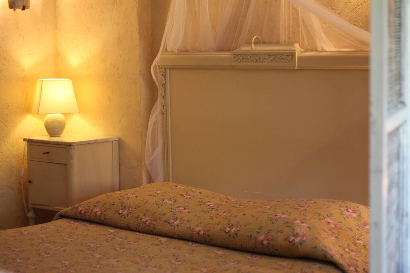 A bedroom with a bed, a bedside table with a lamp, and a canopy bed.