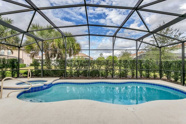 A covered swimming pool with a clear view of the surrounding landscape, including palm trees and houses.