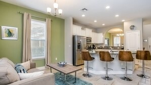 Une cuisine moderne avec des meubles blancs, des appareils en acier inoxydable et un îlot central doté de tabourets de bar.