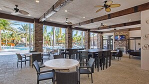 Un espace extérieur aménagé pour les repas, avec des tables et des chaises, une piscine avec un toboggan et des palmiers en arrière-plan.