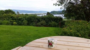 A wooden table with a mug in a garden setting, overlooking a lake and hills. - An Cala - Spacious house with stunning sea-views (Tobermory)