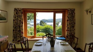 A dining area with a table set for four, a view of a lake and hills, and floral curtains. - An Cala - Spacious house with stunning sea-views (Tobermory)