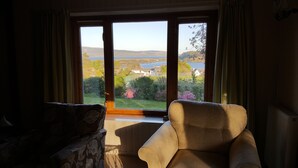 A room with a large window offering a view of a lake and houses. There are two sofas and a radiator. - An Cala - Spacious house with stunning sea-views (Tobermory)