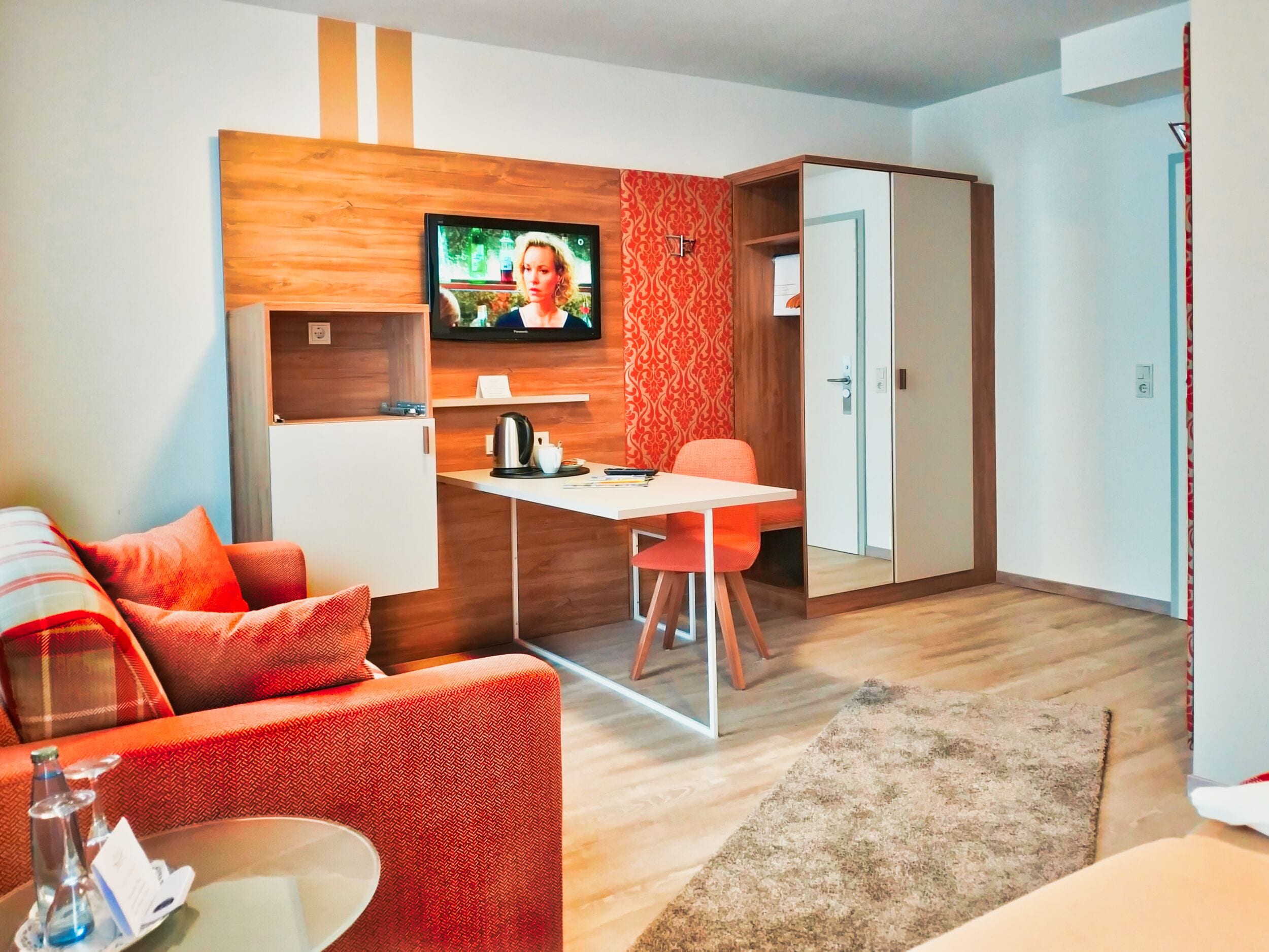 Un espacio habitable compacto con un sofá, una mesa de comedor y un televisor instalado en una pared de madera.