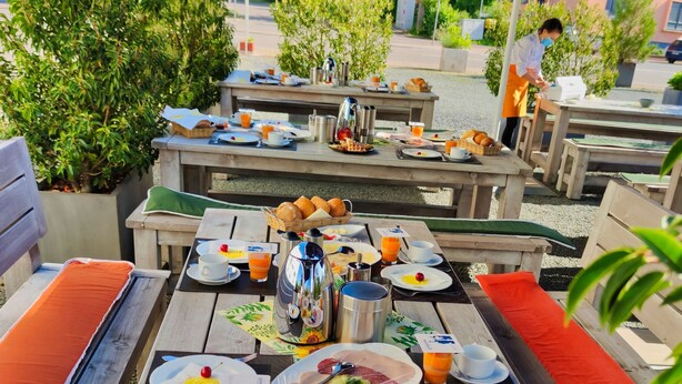 Un área de comedor al aire libre con mesas y bancos de madera, cubierta por un toldo azul.