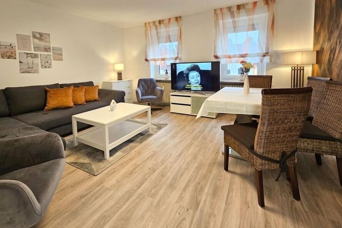 Een moderne woonkamer met een bank, salontafel, televisie en rieten stoelen.