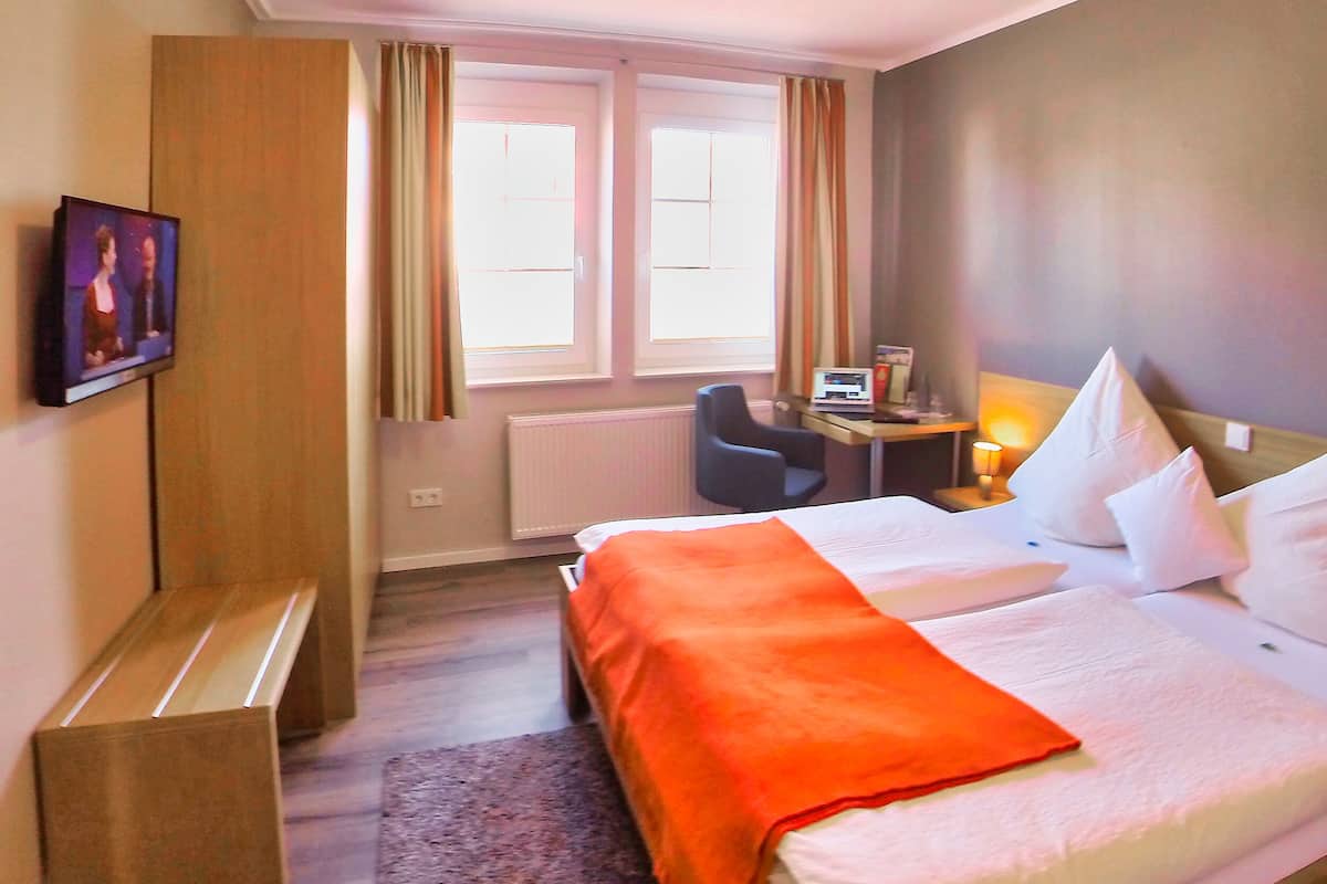 Een hotelkamer met een bed, een bureau met een computer, een stoel en een raam met gordijnen.