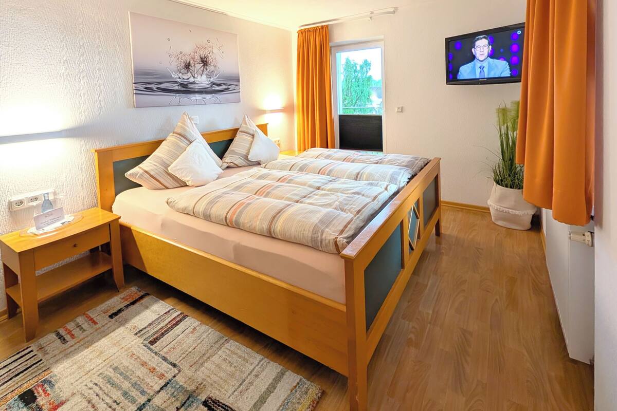Een hotelkamer met een bed, nachtkastje, televisie en een raam met gordijnen.