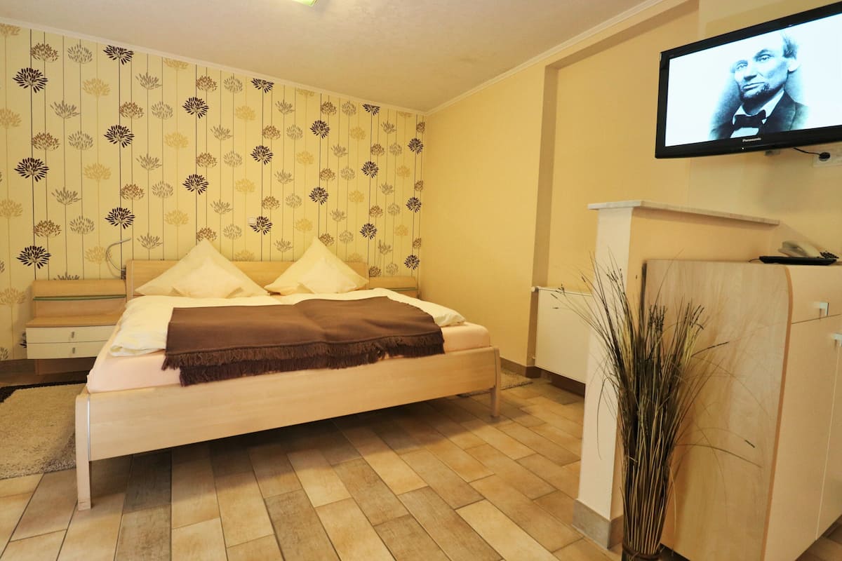 Een slaapkamer met een bed, een aan de muur bevestigde televisie en een houten kast.
