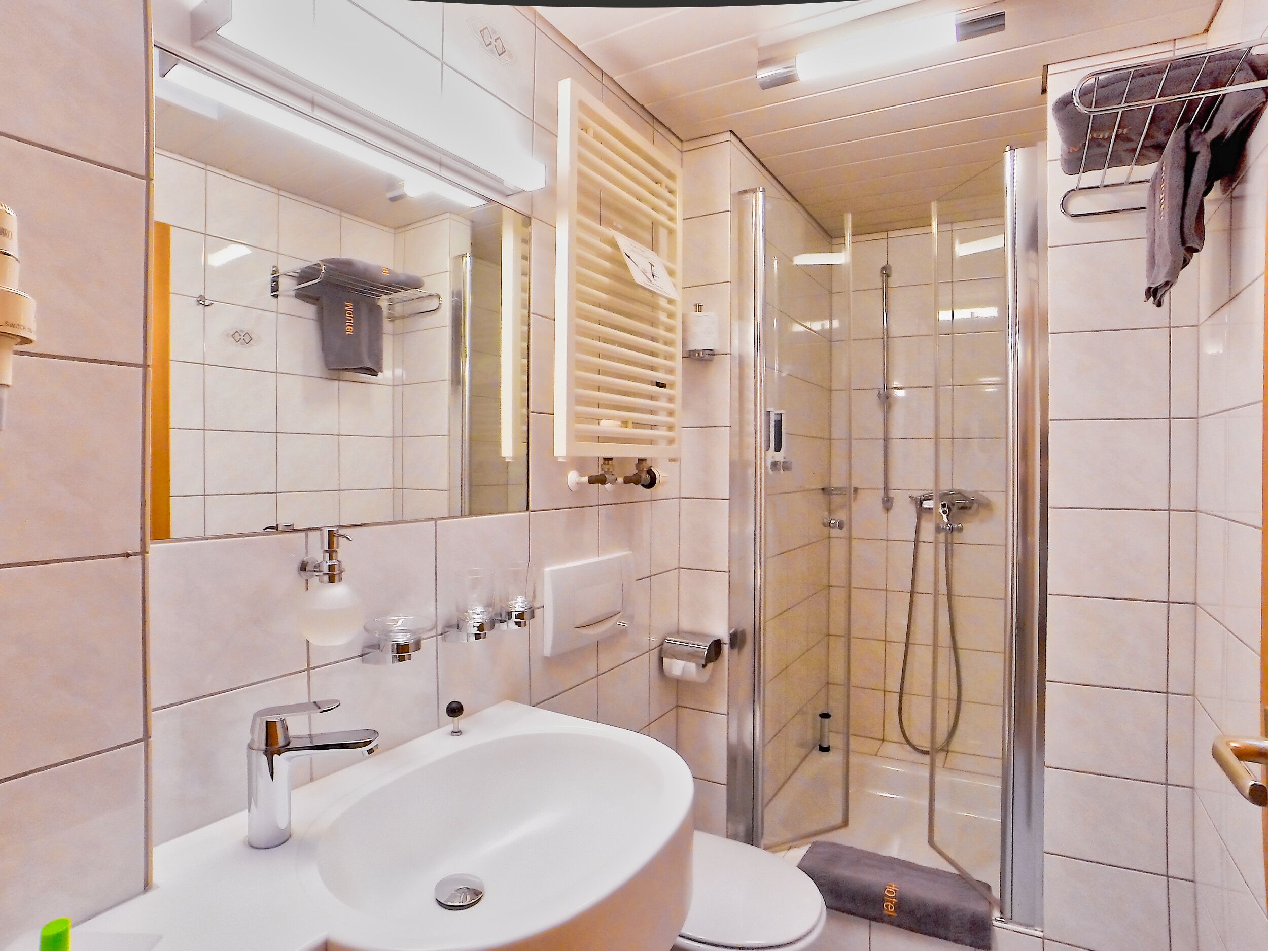 Un baño moderno con lavamanos, espejo, toallero y ducha con mampara de vidrio.