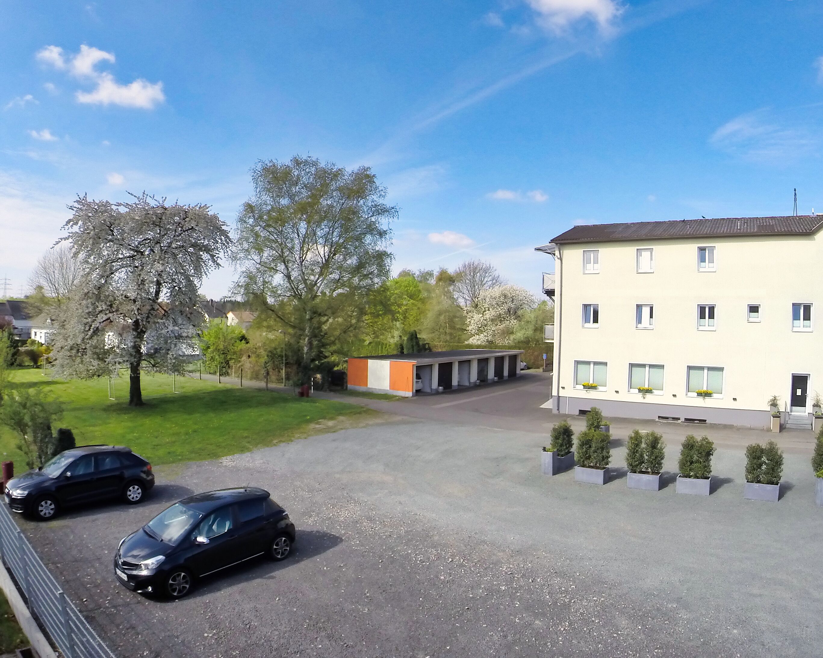 A parking area with two cars, a building with multiple windows, and a small orange structure.
