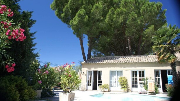 A building with a tiled roof, a swimming pool, and a large tree in front.