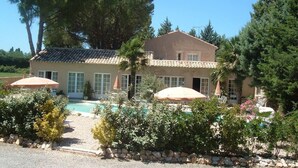 A two-story house with a swimming pool, surrounded by lush greenery and a stone pathway.