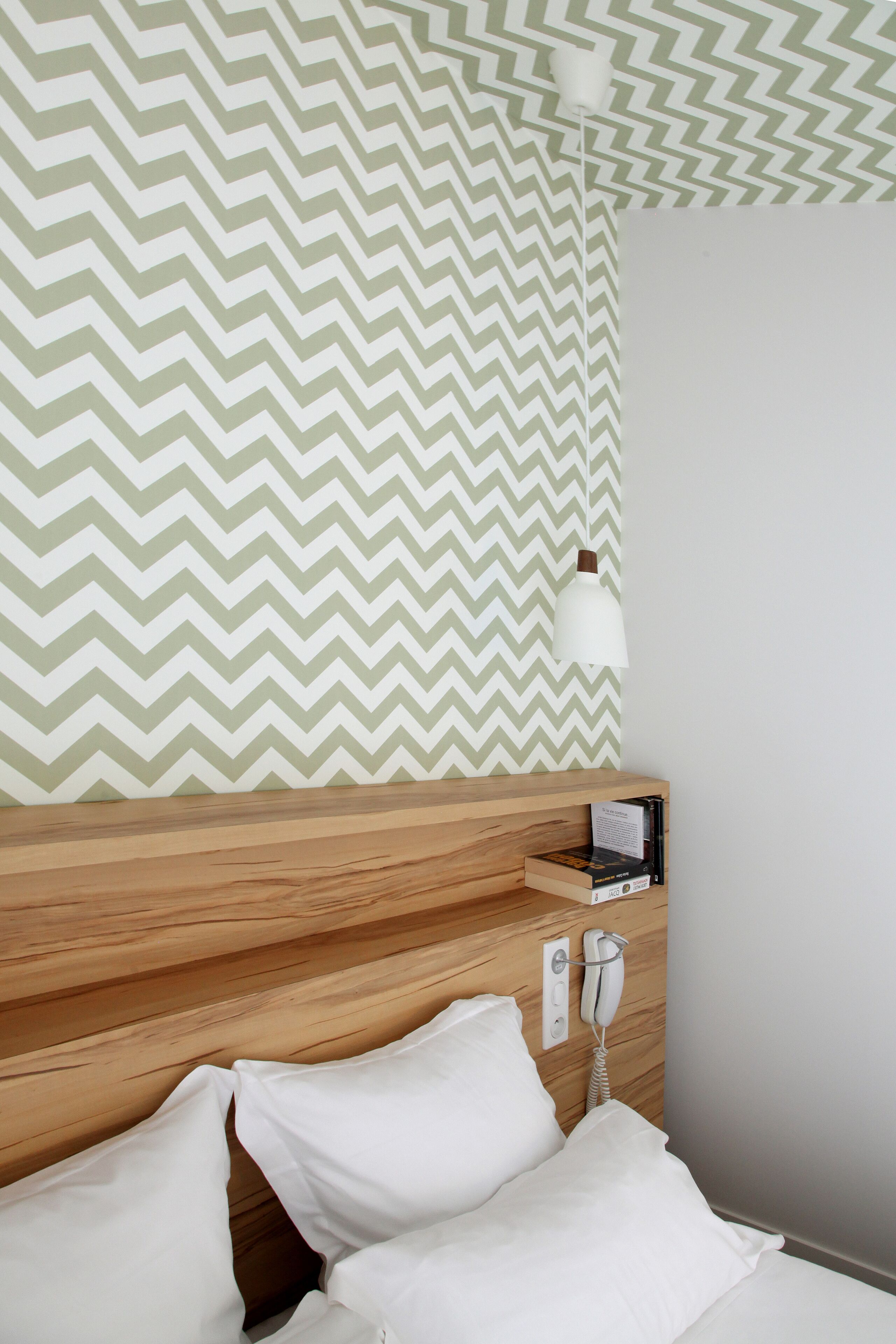 Une chambre d’hôtel avec une tête de lit en bois, un lit blanc avec des oreillers, un téléphone et un mur orné d’un motif en chevrons.
