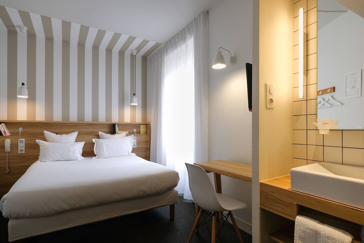 Una habitación de hotel con cama, escritorio, silla, espejo y teléfono instalado en la pared.
