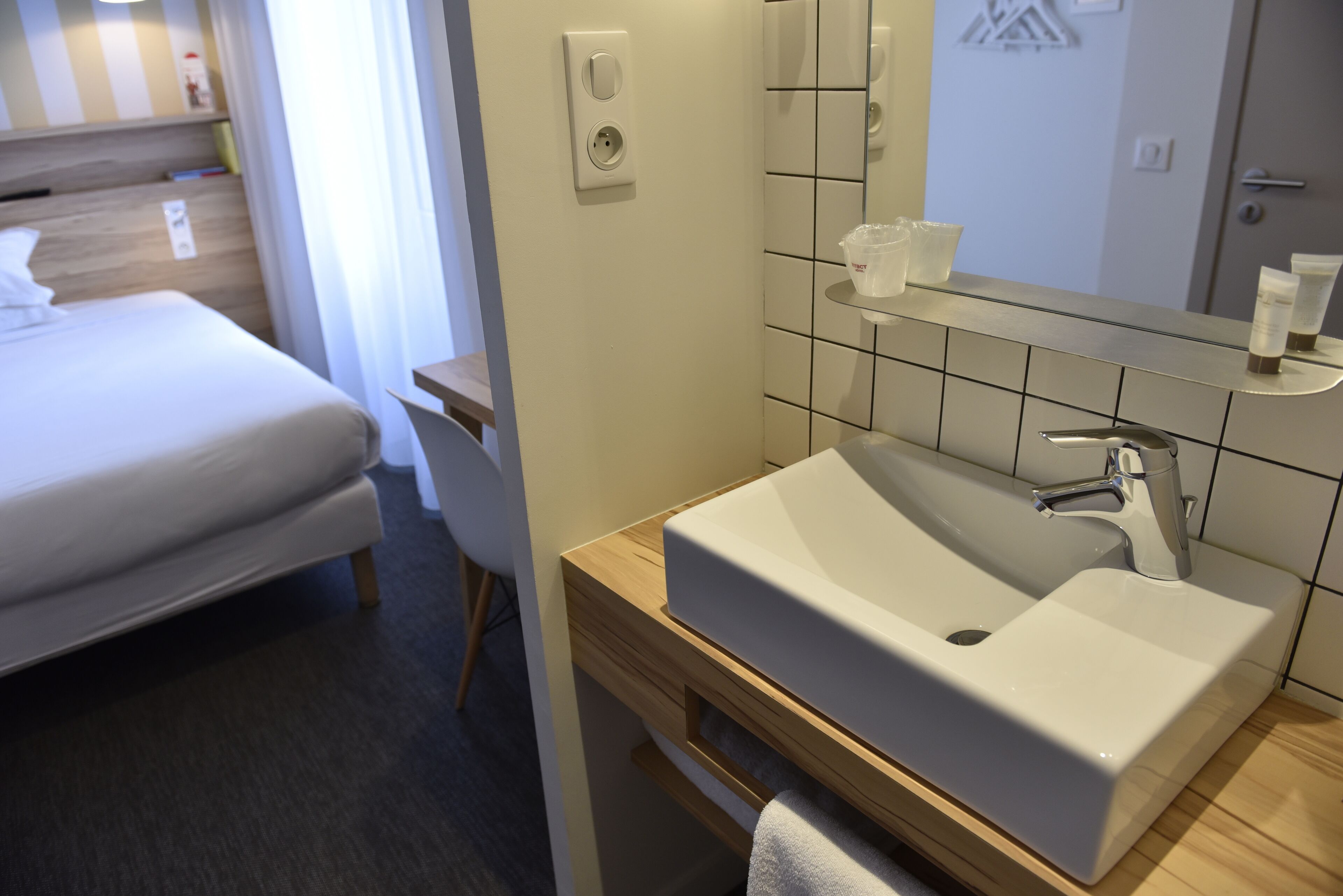 Quarto de hotel com uma cama, uma mesa de cabeceira de madeira, uma pia e um espelho.
