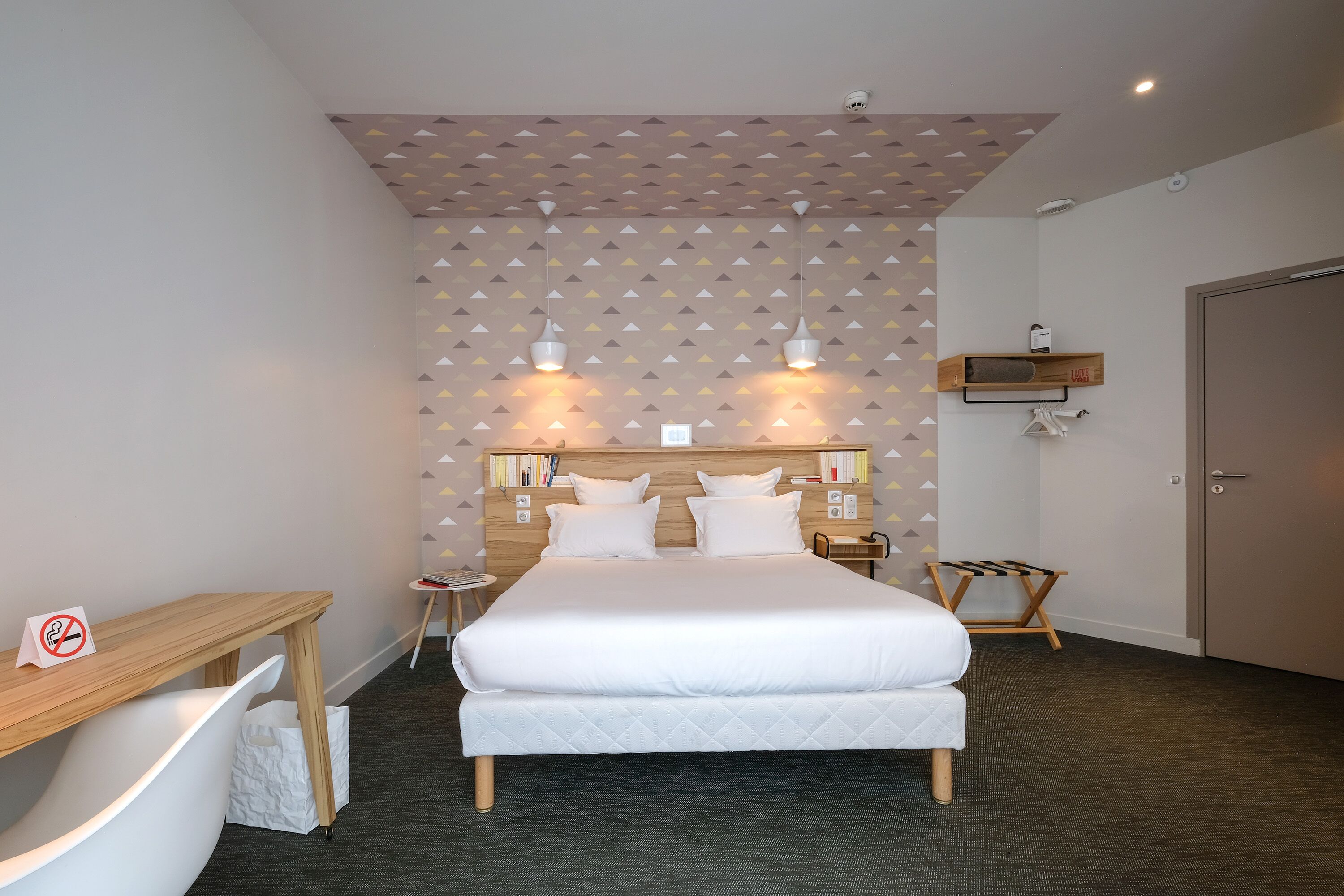 Una habitación de hotel ordenada con una cama, mesitas de noche, un escritorio y una silla.