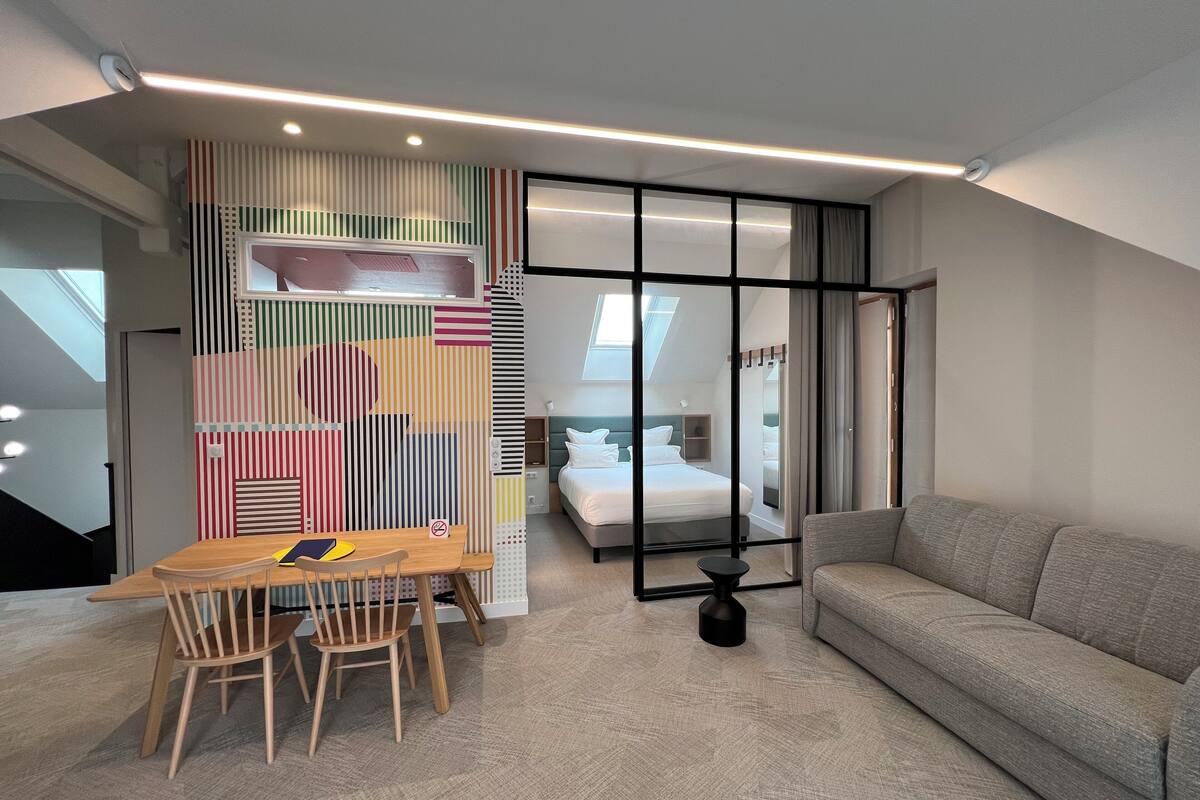 Una habitación de hotel moderna con zona de comedor, sofá y cama.