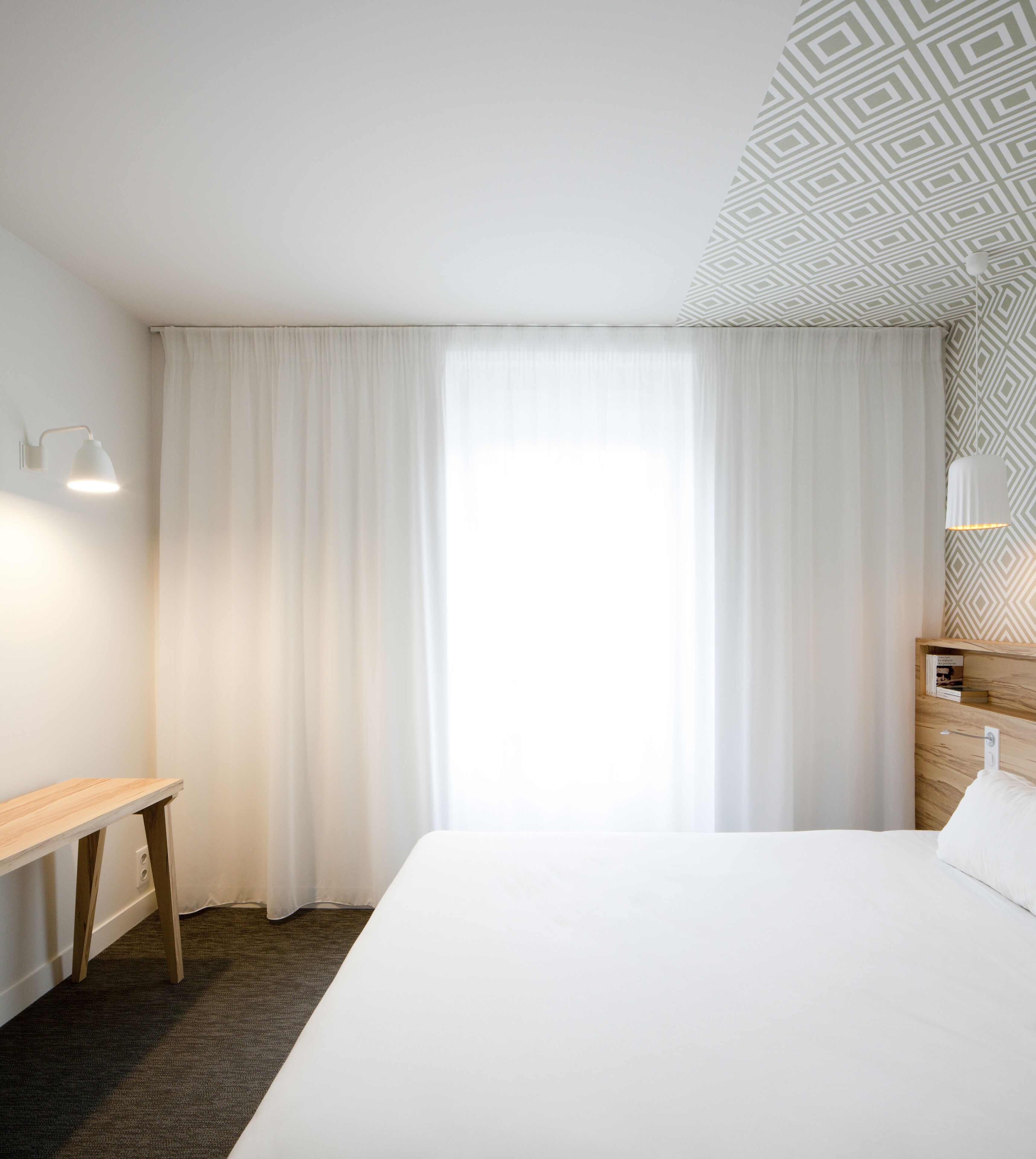 Habitación de hotel con una cama grande, una mesita de noche de madera, un escritorio y un papel tapiz estampado.