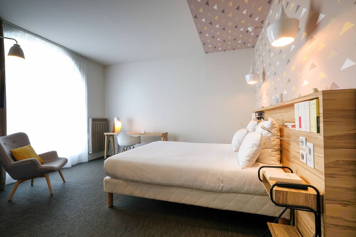 Una habitación de hotel con una cama, un escritorio, una silla y una lámpara.