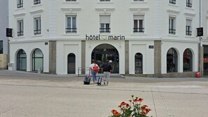 Un bâtiment blanc avec une enseigne indiquant « hôtel marin ». Il possède de nombreuses fenêtres et une grande entrée avec une porte en verre.