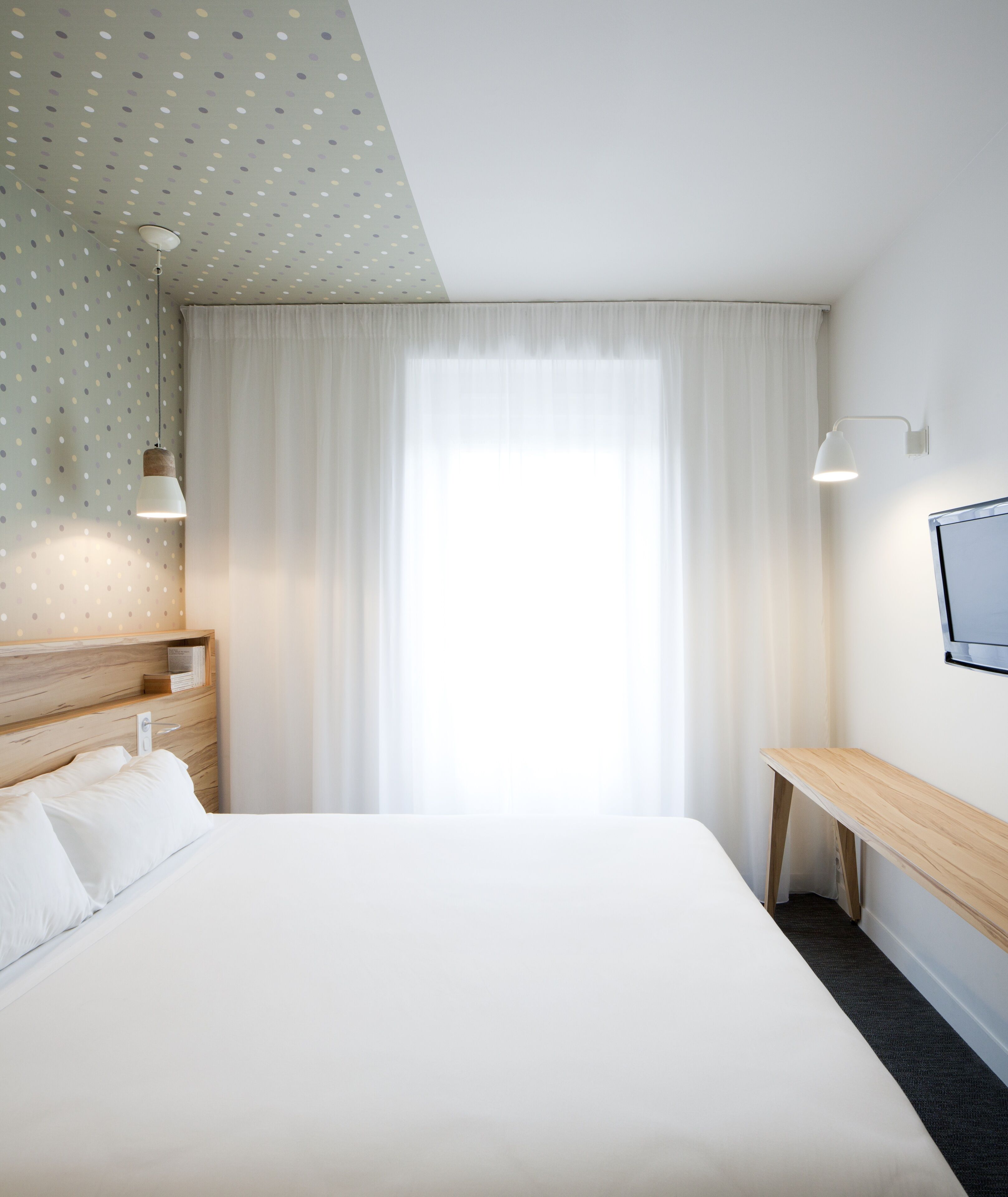 Ein Hotelzimmer mit einem großen Bett, einem Holz-Kopfteil, einem Schreibtisch und einem an der Wand montierten Fernseher.