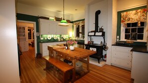 A kitchen with wooden flooring, a wooden table, a bench, white cabinets, a green wall, and a window with floral curtains. - Beautiful Setting, Romantic Historic Arts & Crafts Home, Great Longs Peak Views (Estes Park)