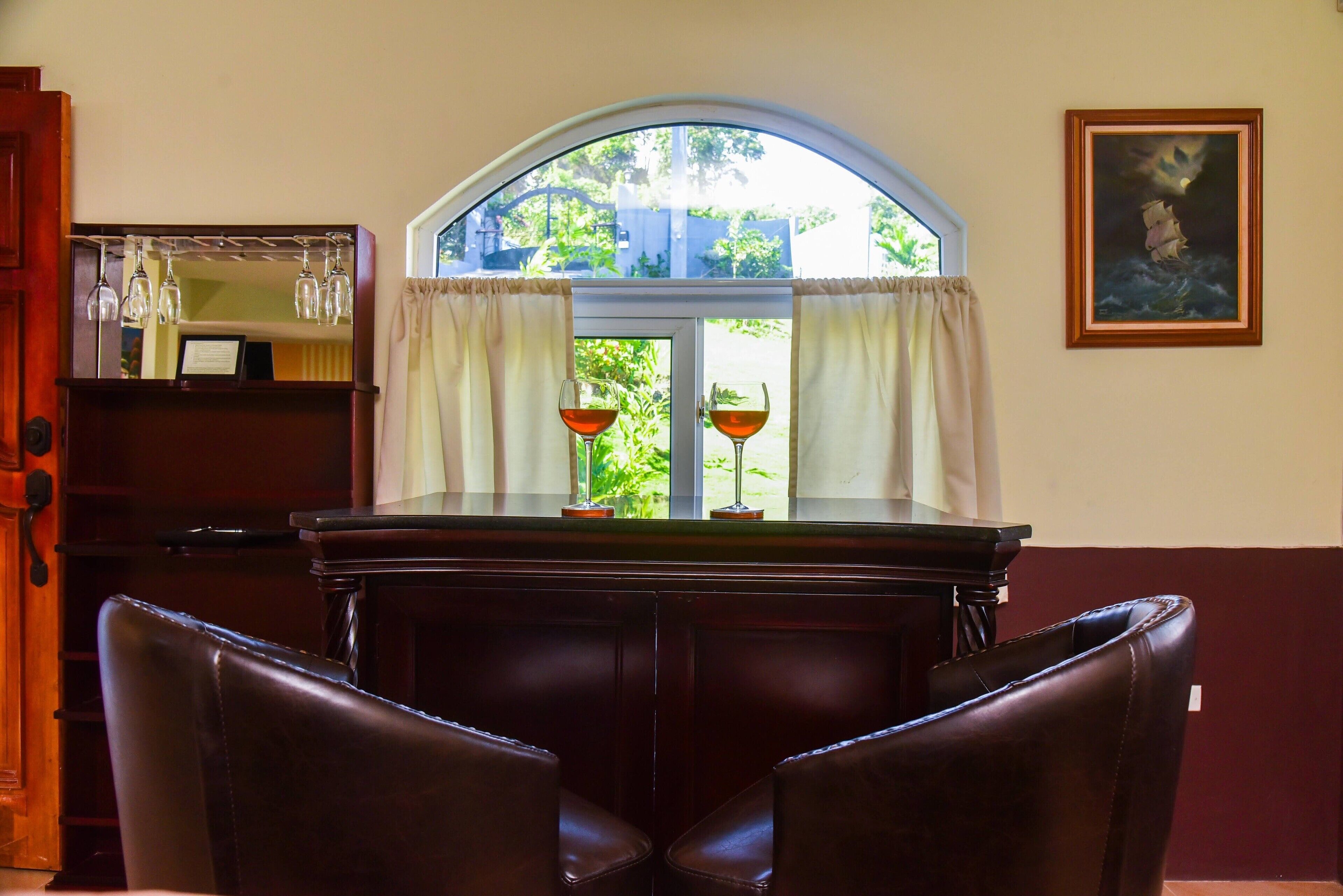 A room with a dark wooden table, two leather chairs, a window with curtains, and a framed picture on the wall.