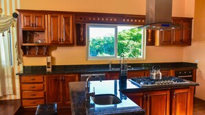 A kitchen with wooden cabinets, a large window, a stainless steel sink, and a gas stove.