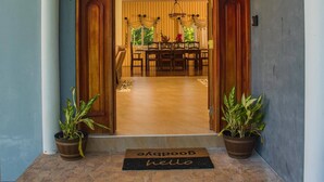 A grand entrance with a stone archway, a wooden door, and a doormat. Inside, there is a dining area with a chandelier and striped curtains.
