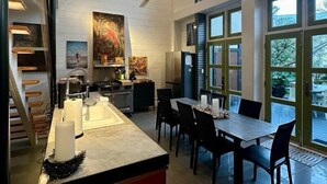 Une cuisine moderne dotée d’un îlot central, d’un coin repas avec des chaises, de grandes fenêtres et d’un ventilateur de plafond.