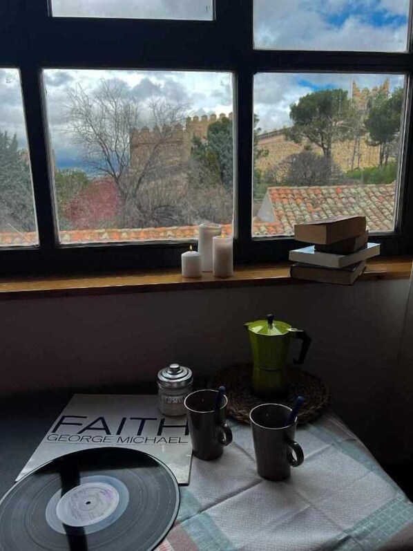 A room with a window overlooking a scenic landscape, a table with a vinyl record, a coffee maker, and a mug.