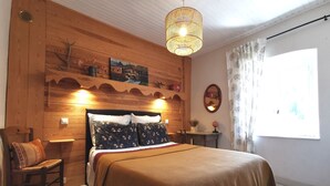 A cozy bedroom with a wooden headboard, a large bed with a brown blanket, a wicker hanging light, and a window with curtains. - The house under the stars (Sembadel)