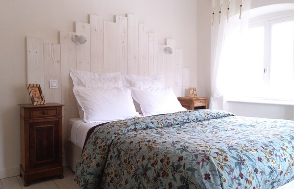 A bedroom with a bed, a wooden nightstand, a small cabinet, and a window with curtains.