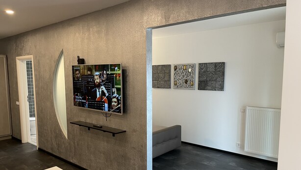 Un interior moderno con un televisor de pantalla plana montado en una pared texturizada, un sofá gris y tres obras de arte abstracto.