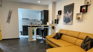 Una sala de estar moderna con un sofá amarillo y una cocina al fondo.