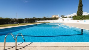 Una piscina con agua azul cristalina, rodeada por un muro blanco y un seto.